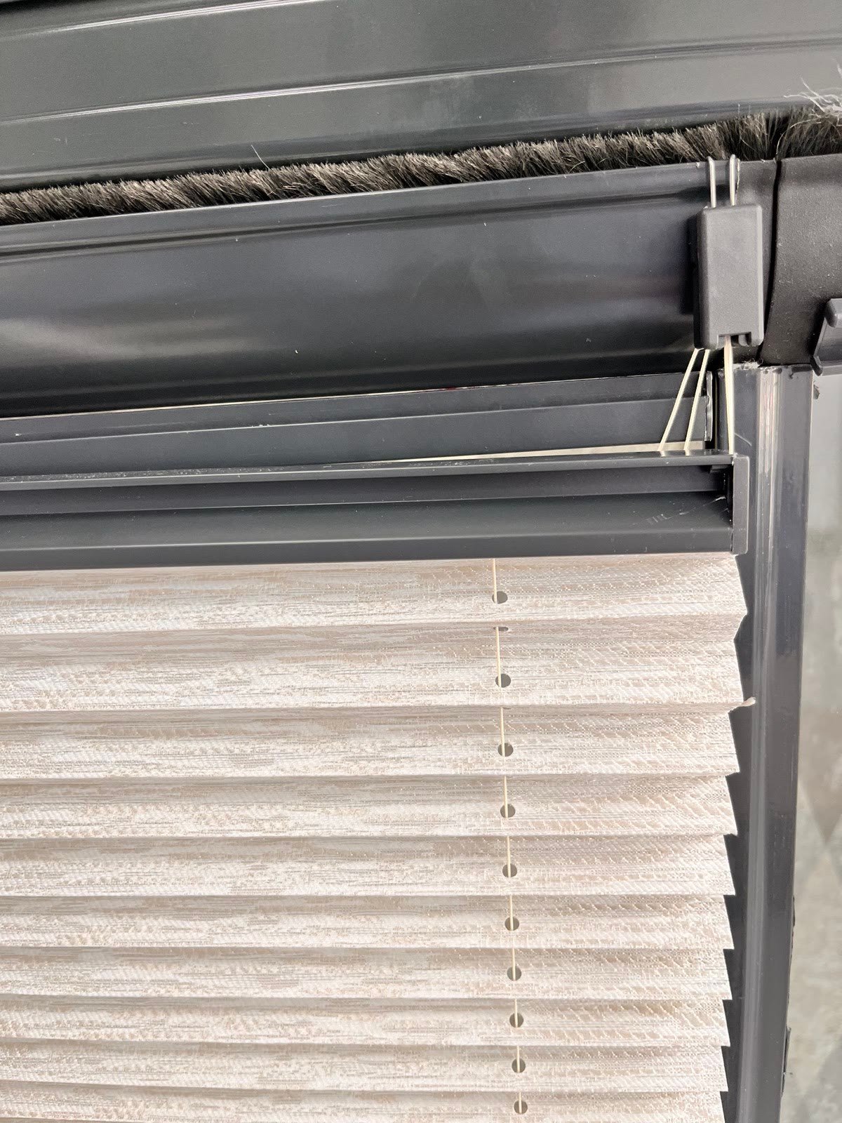 Cam balkon profilini üstten kavrayan siyah metal kancalı plise perde aparatı